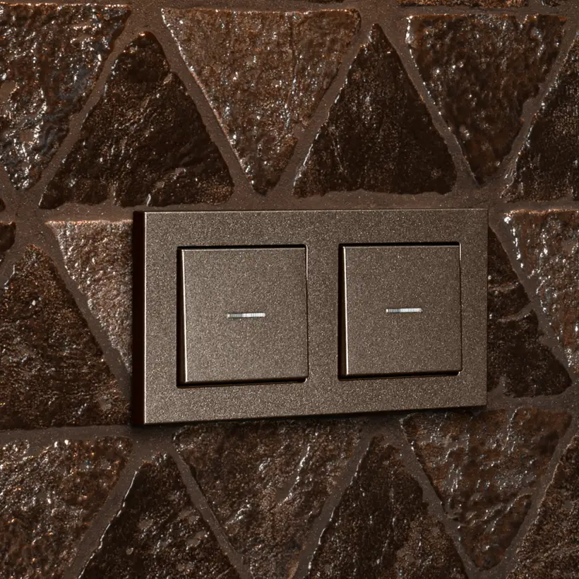 JUNG A 550 two-gang rocker switch in bronze on a textured ceramic wall