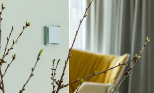 Light green JUNG LS 990 switch beside a window and a yellow armchair