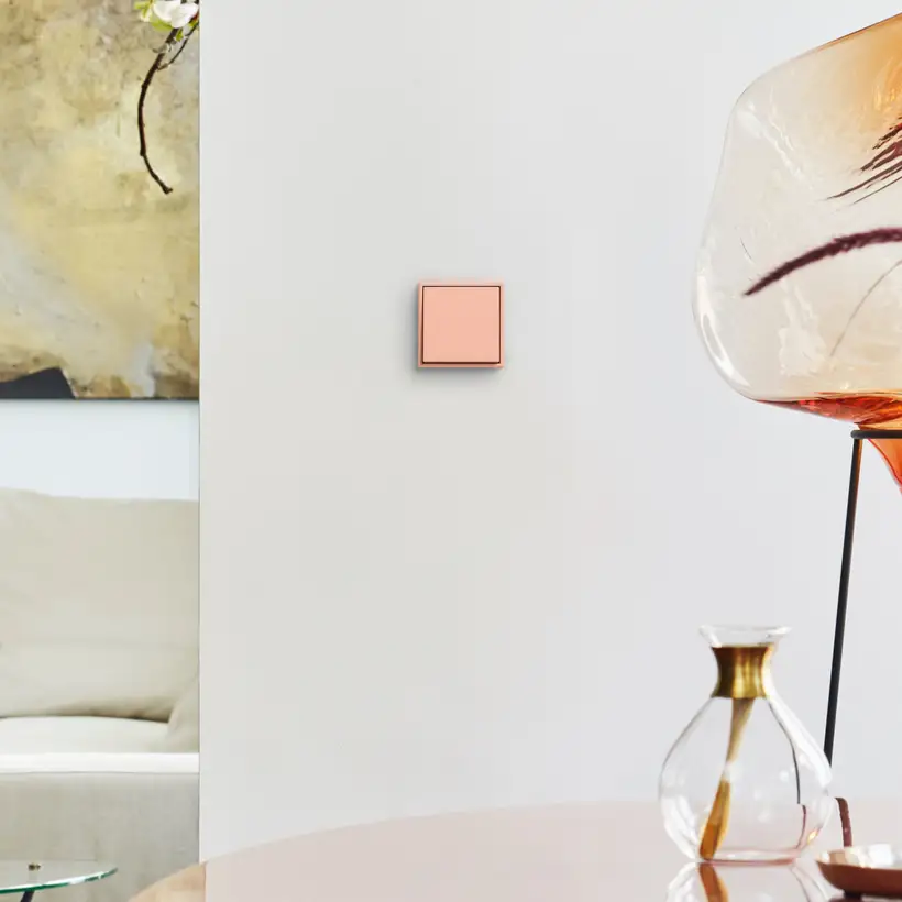 Pale rose JUNG LS 990 switch on a light wall beside a glass vase