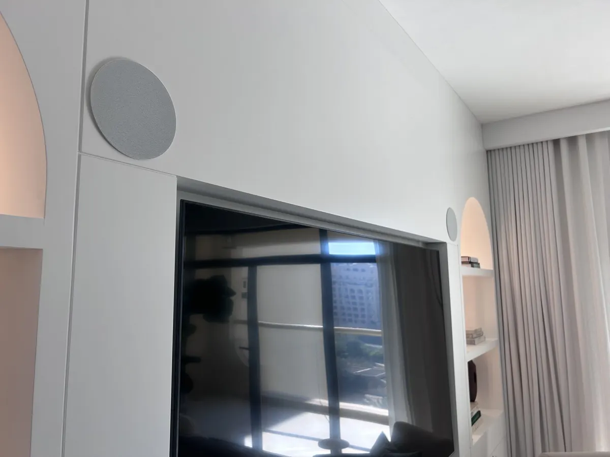 Two Artsound on-wall speakers flanking a TV as front channels in a home cinema setup