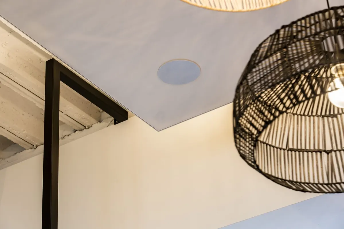 Flush round Artsound in-ceiling speaker in a finished ceiling beside a woven pendant light