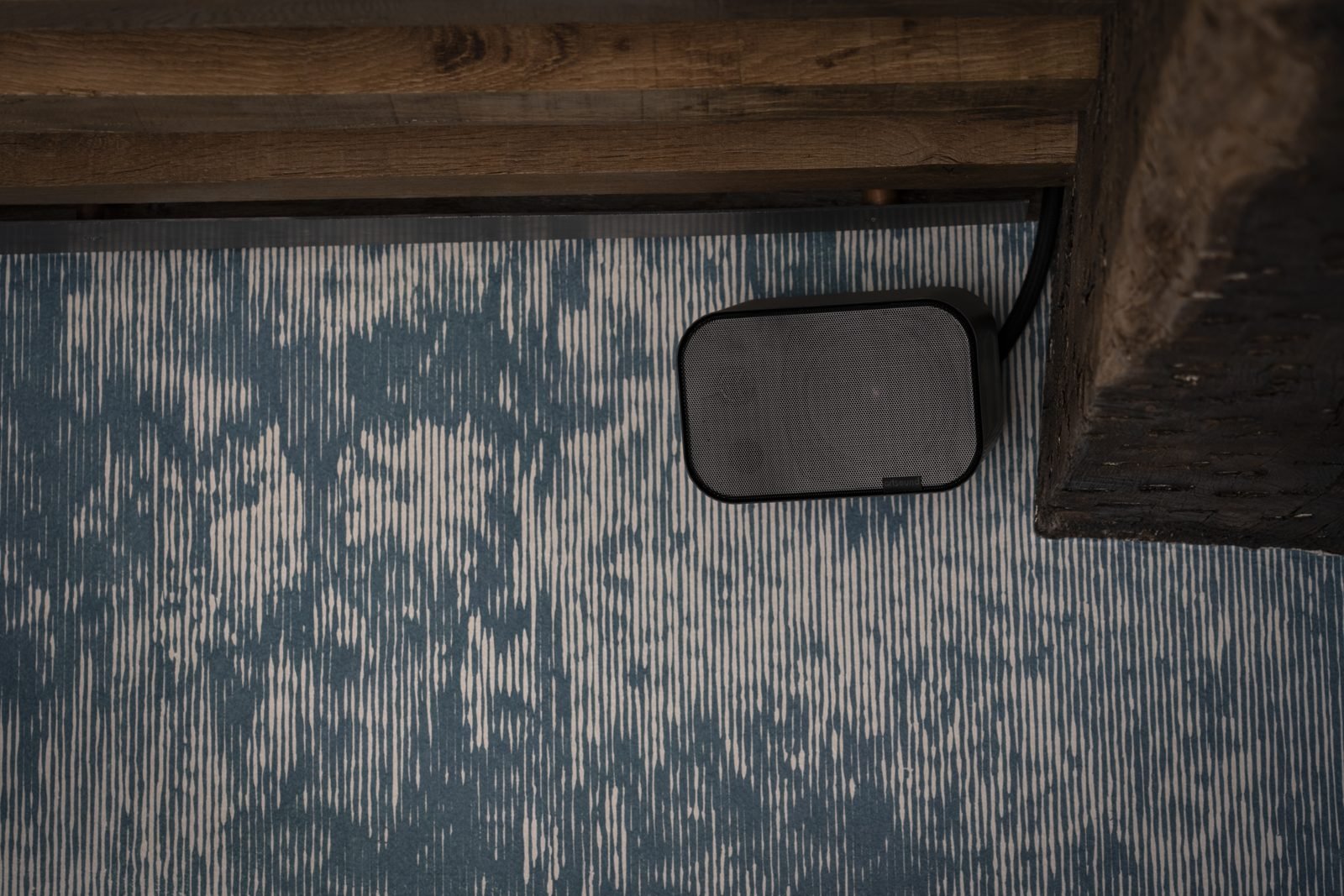 Black Artsound surface-mount speaker on a wall with its cable running up out of sight