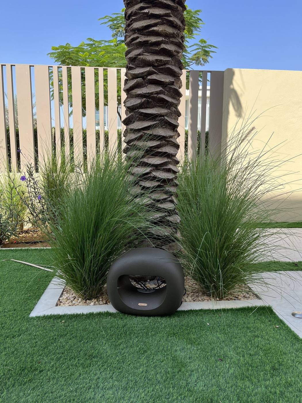 Artsound outdoor speaker installed at the base of a palm tree in ornamental grass landscaping