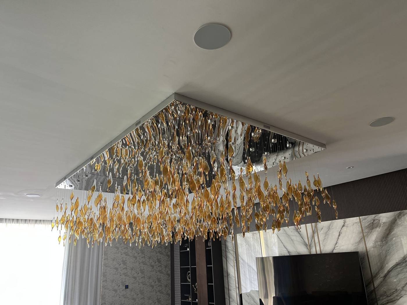 In-ceiling Artsound speaker beside a gold blown-glass chandelier in a villa living room